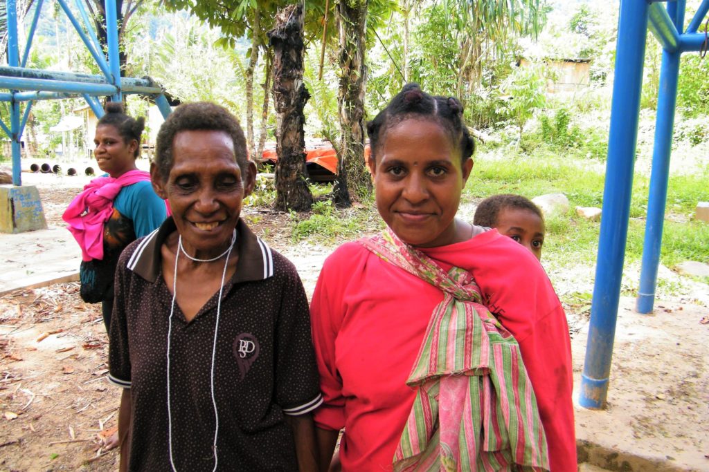 Three Papuan ladies with kids of a village smiling at the camera