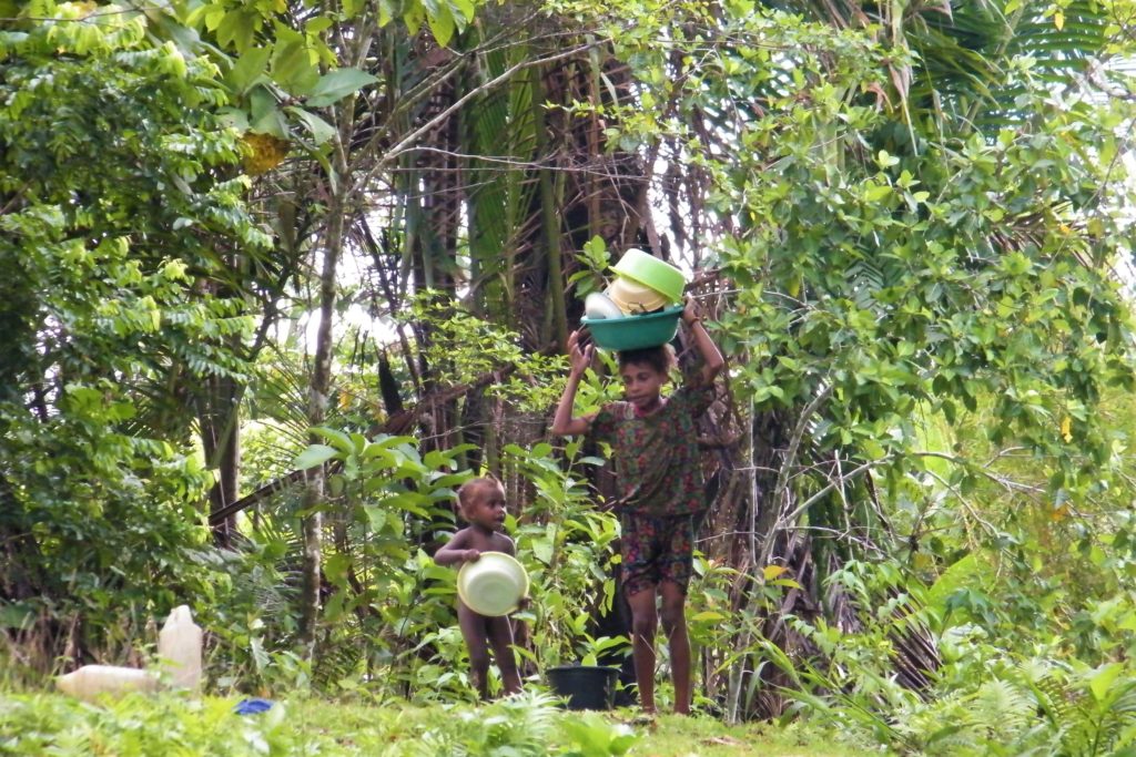 Two kids preparing to wash dishes at a river in West Papua