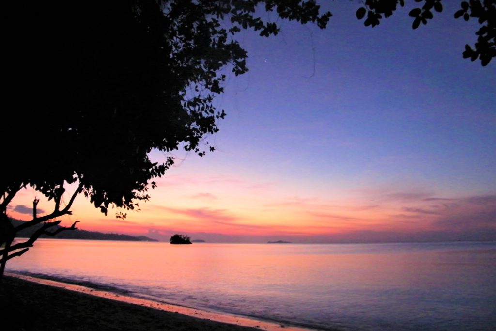 Sunset from a beach in Raja Ampat with a little island in the background